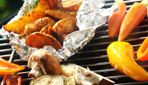 Close-up of potatoes being grilled in foil along with other vegetables.