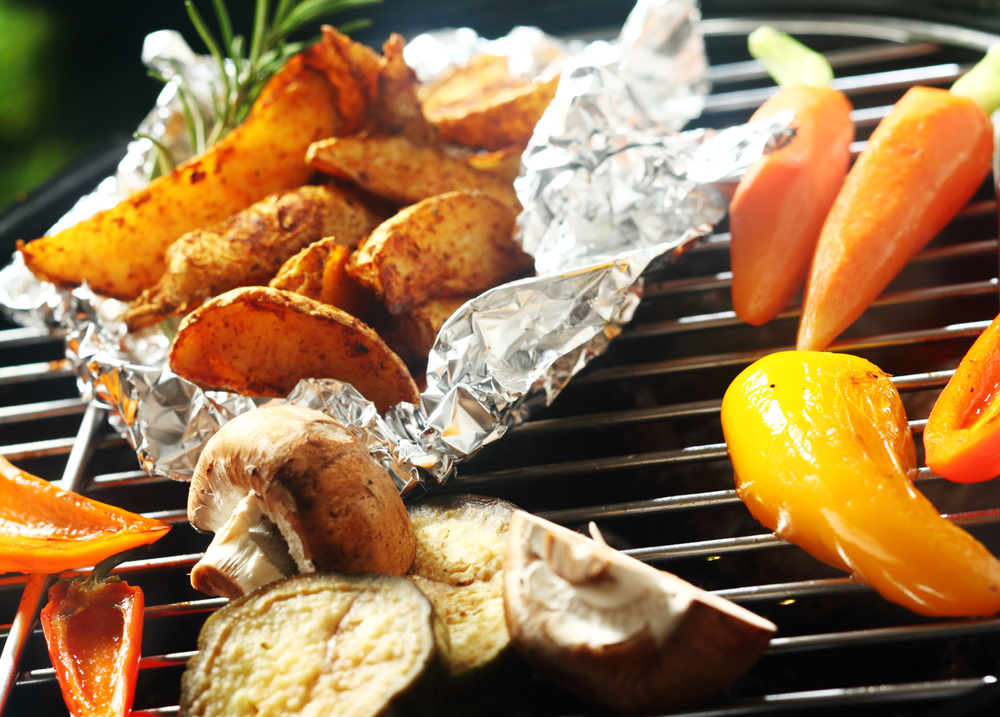 Close-up of potatoes being grilled in foil along with other vegetables.