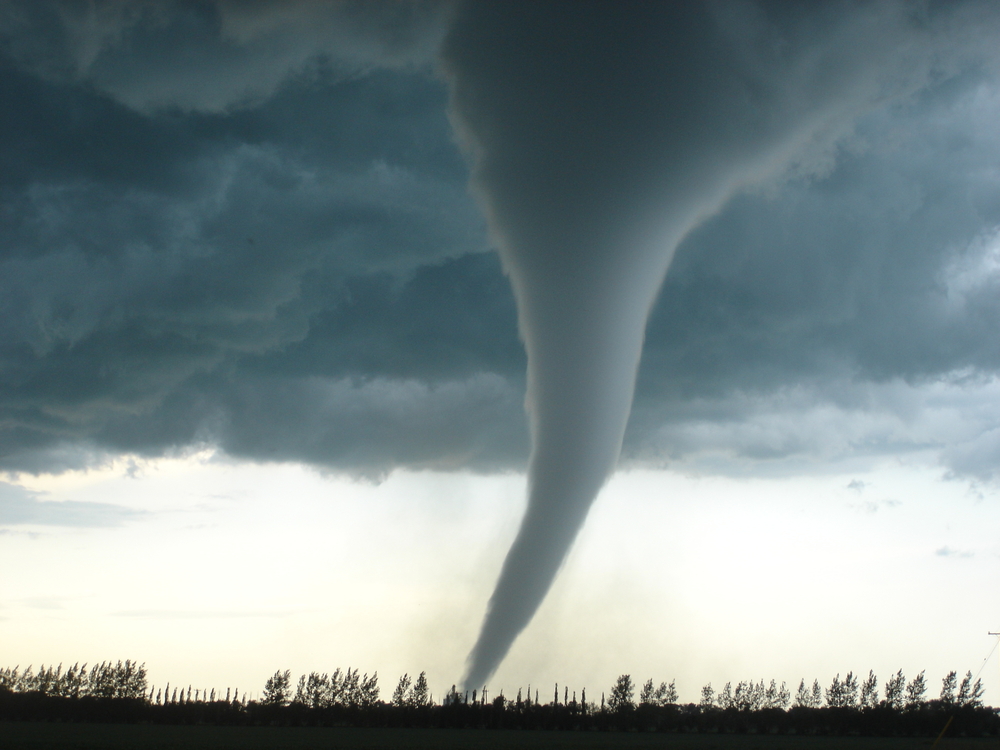 Dark grey tornado touching down in an empty field.