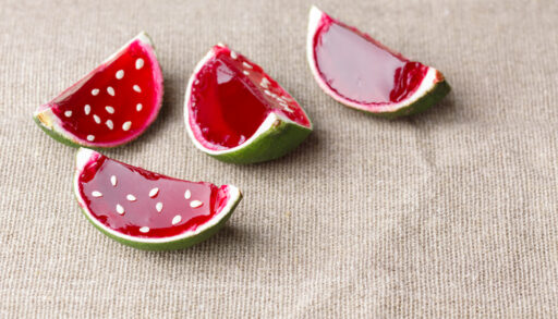 Close-up of watermelon jello shots made with lime rinds on a linen tablecloth.