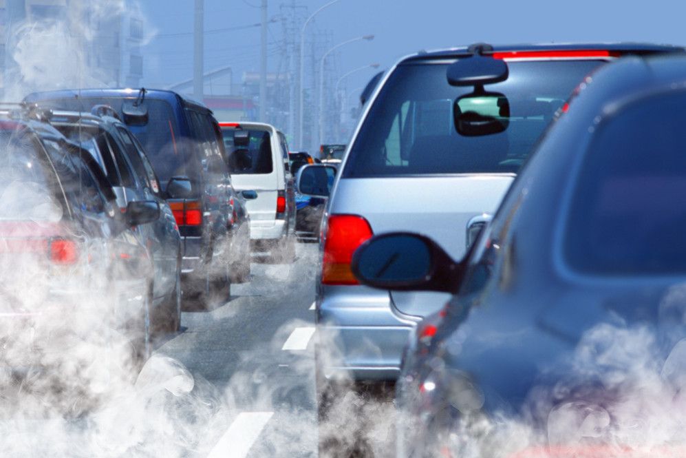 Cars lined up on a roadway with exhaust blowing in the air.