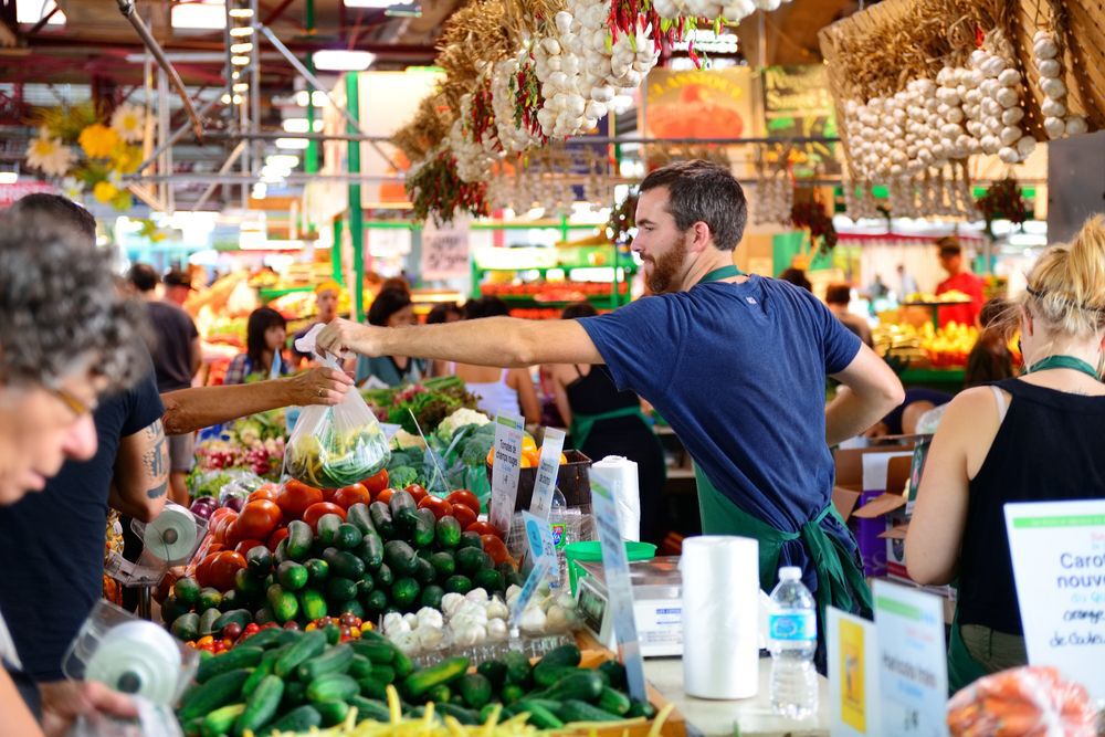 Man handing a bag of produce to a customer at a farmers' market.
