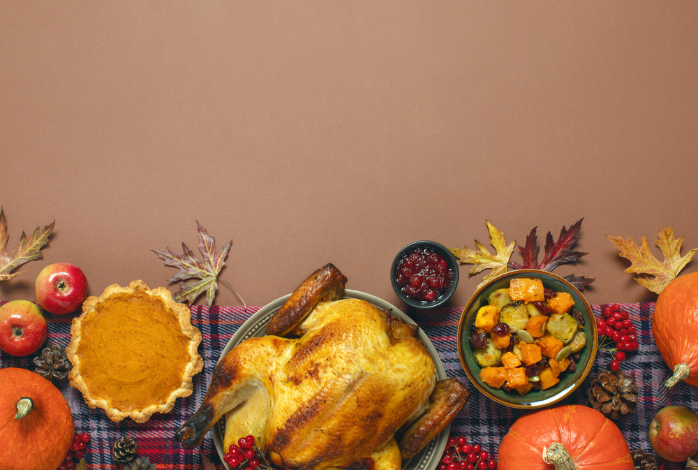 Flatlay image of a Thanksgiving table with a turkey, pumpkin pie, vegetables, cranberry sauce and pumpkins.