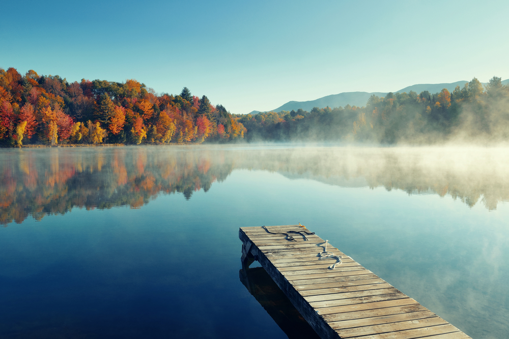 Wooden dock on a lake surrounded by red trees with some fog hovering above the water.