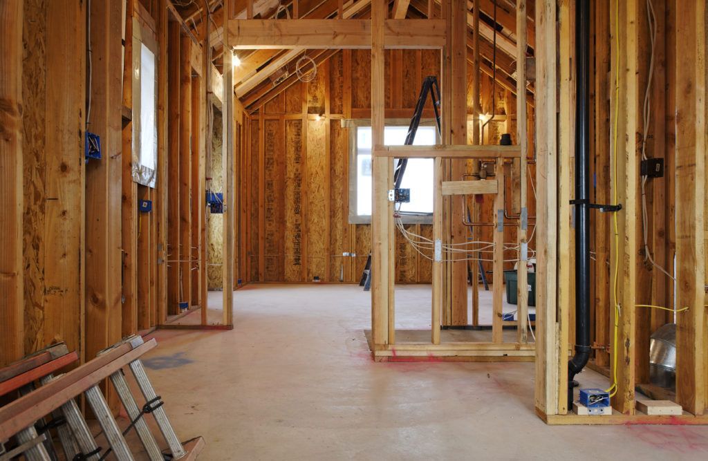Home interior stripped down to its studs during construction, with exposed wires and a ladder on the floor.