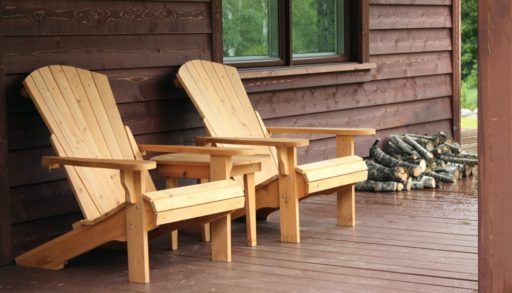 Dark brown porch with two light-coloured Muskoka chairs covered in rain drops.