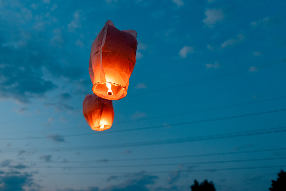 Two red paper lanterns floating in the sky at dusk.