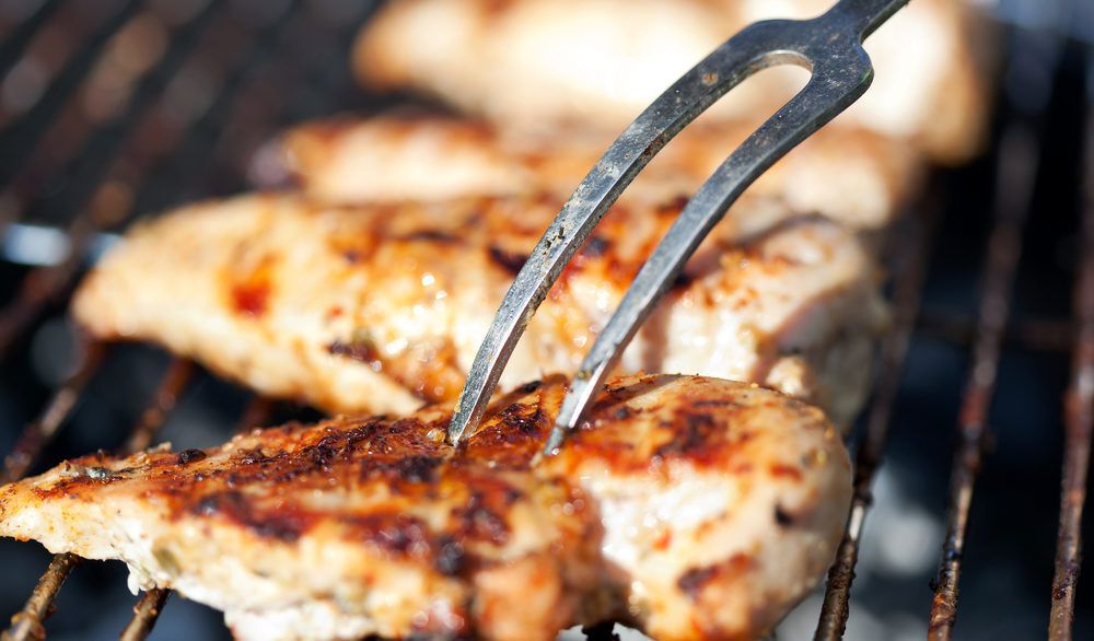 A two-pronged fork stabbing a grilled chicken breast.