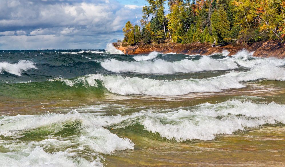 Blue and green waves crashing on the shores of Lake Superior with a green forest surrounding the water.