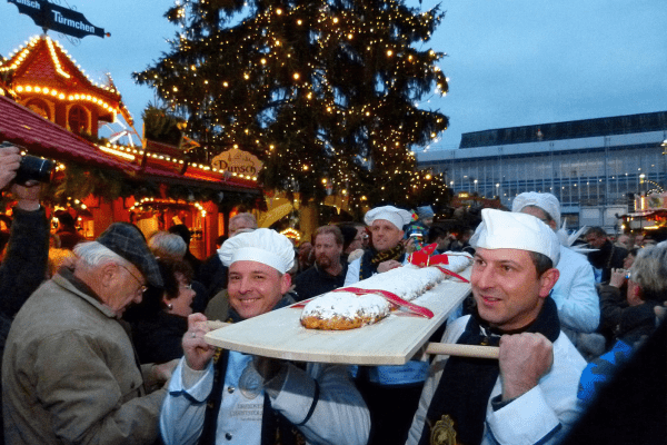 Several men carrying a long stollen loaf on a board