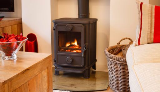 A black wood stove in a living room next to a sofa and a basket for firewood.