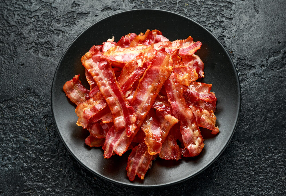 Overhead view of crispy bacon on a black plate.