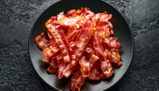 Overhead view of crispy bacon on a black plate.