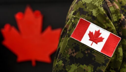Close-up of a Canadian flag patch on a soldier's military uniform with a red maple leaf in the background.