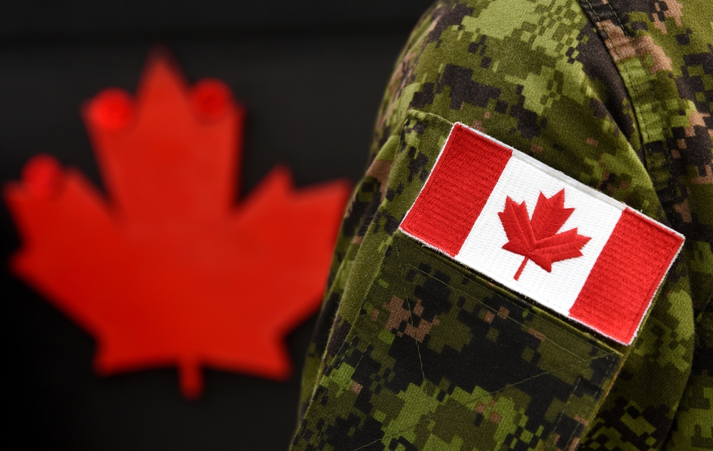 Close-up of a Canadian flag patch on a soldier's military uniform with a red maple leaf in the background.
