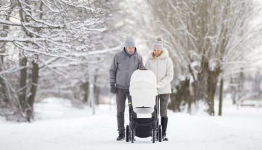 A young couple pushing a stroller through a snow-covered street.