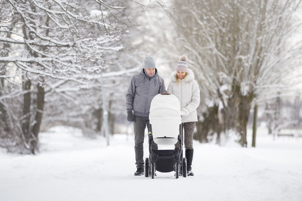 A young couple pushing a stroller through a snow-covered street.
