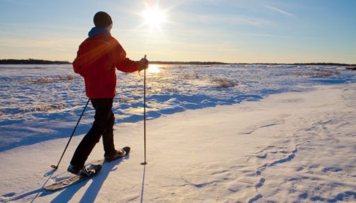 A man in a red coat cross-country skiing with the sun shining in the background.