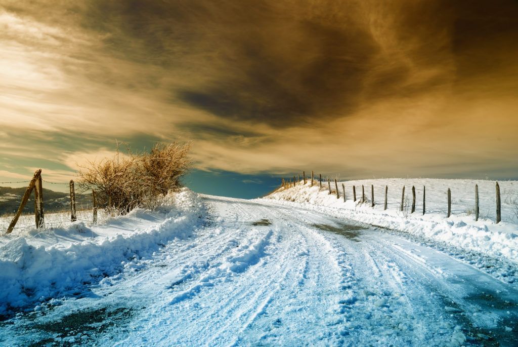 A snow-covered country road with a yellow sky at sunset.
