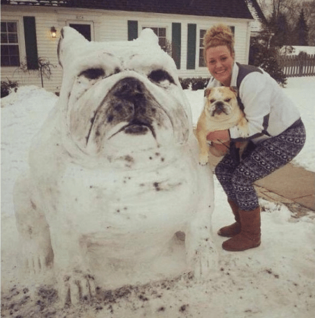 A bulldog snowman next to a woman holding a bulldog