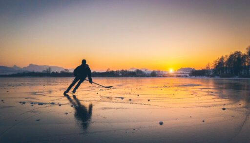 Person with hockey stick skating on frozen lake at sunset.