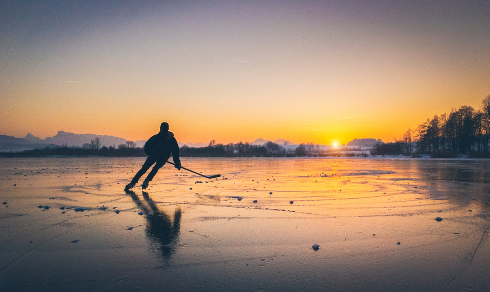 Person with hockey stick skating on frozen lake at sunset.
