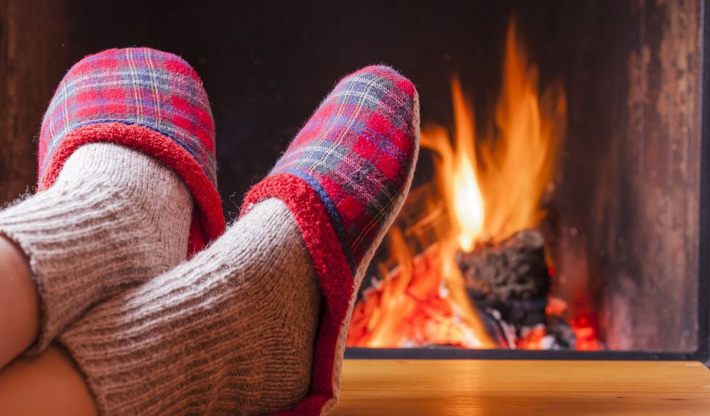 Close-up of a person's feet with plaid slippers relaxing by the fire.
