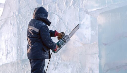 Person in winter clothes carving ice with a chainsaw.