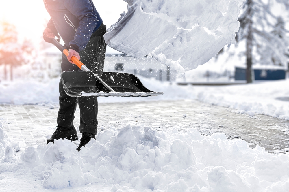 Close-up of someone shovelling snow from their driveway with a black shovel.
