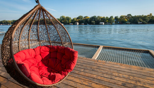 Red cushioned hammock overlooking a lake with trees in the background.