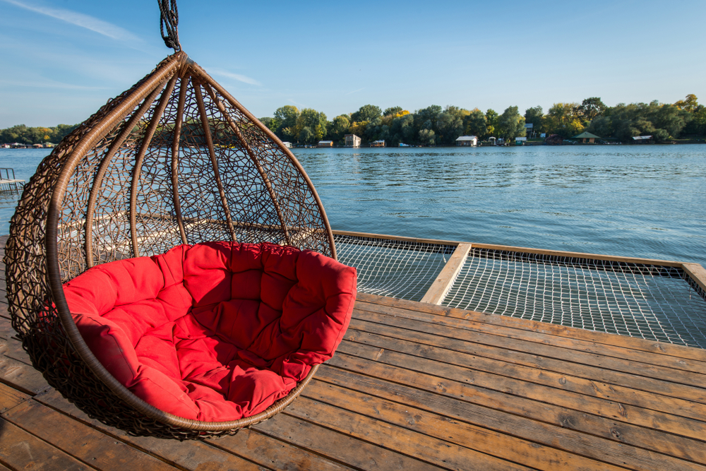 Red cushioned hammock overlooking a lake with trees in the background.