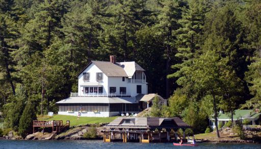 A large white, lakeside home surrounded by trees.