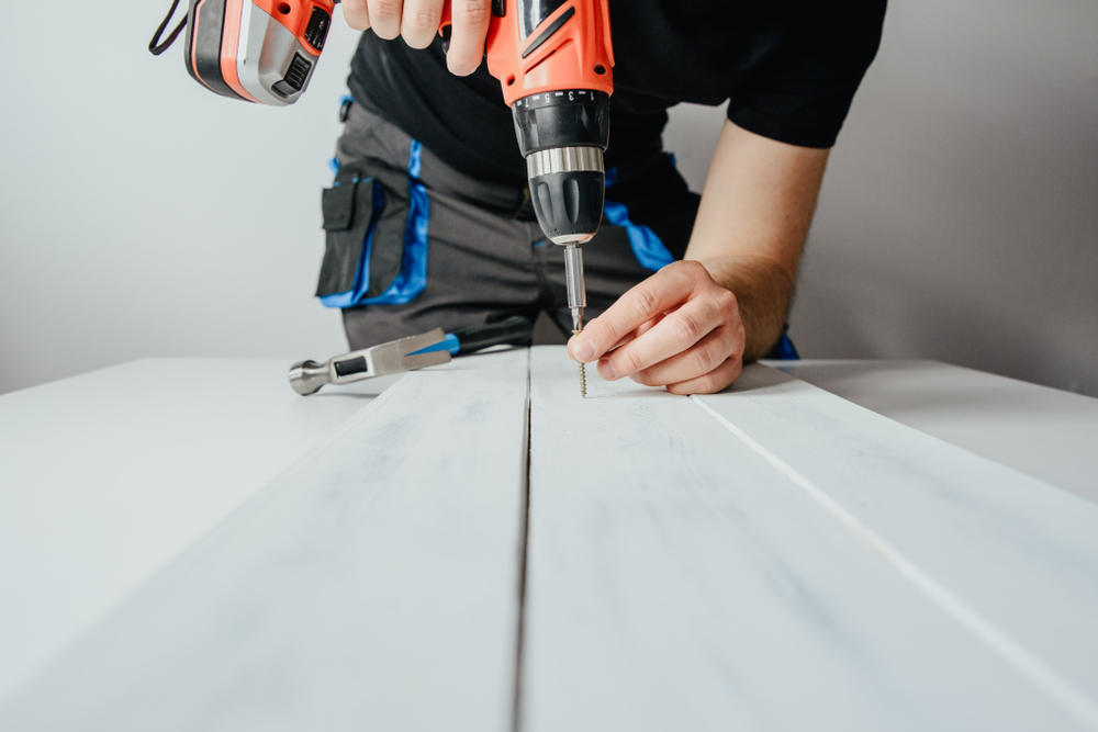 Person screwing a screw into a white board.