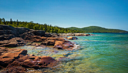 Rocky shoreline of Lake Superior against forest landscape.