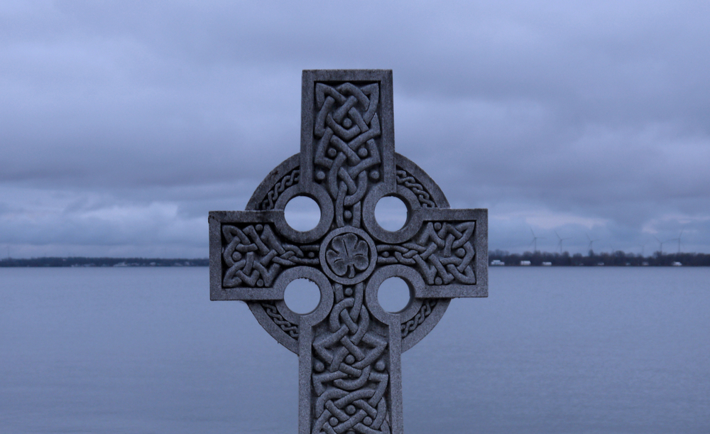 Close-up of celtic cross overlooking a body of water at dusk.