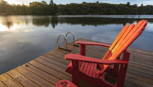 Two red chair facing a sunset on a dock overlooking a lake.