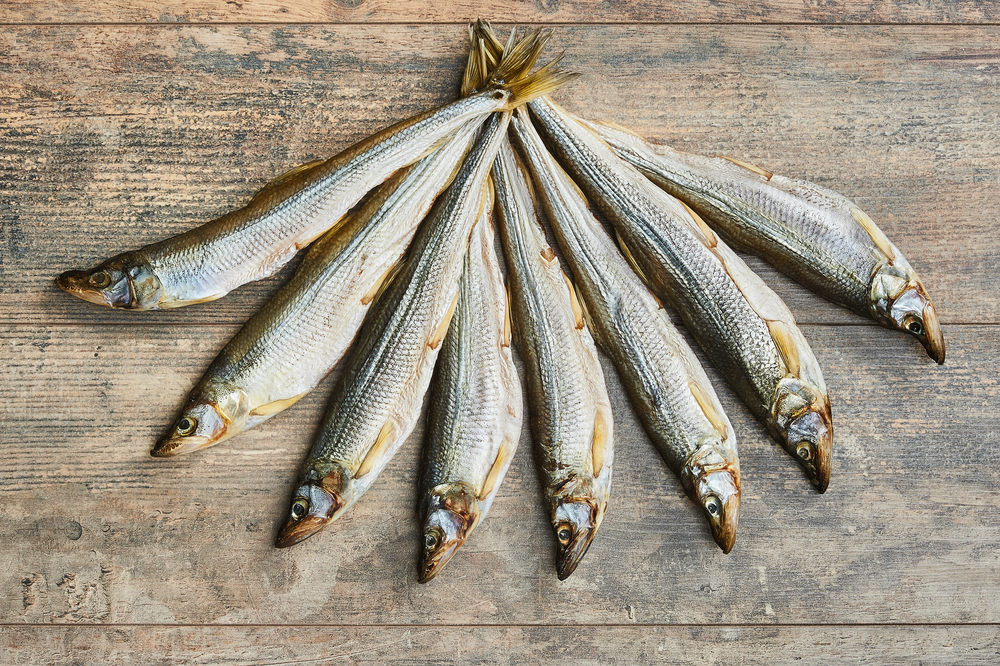 Eight rainbow smelt fish on a wooden board.