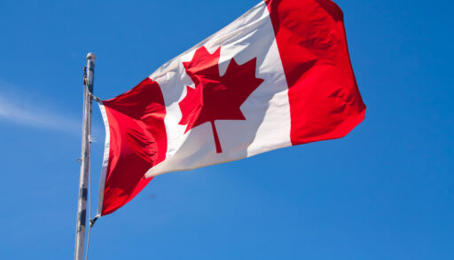 The Canadian flag waving in the wind against a blue sky.
