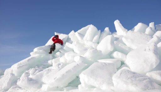 Pileup of ice shove on a shoreline with a kid in a red coat sitting on it.