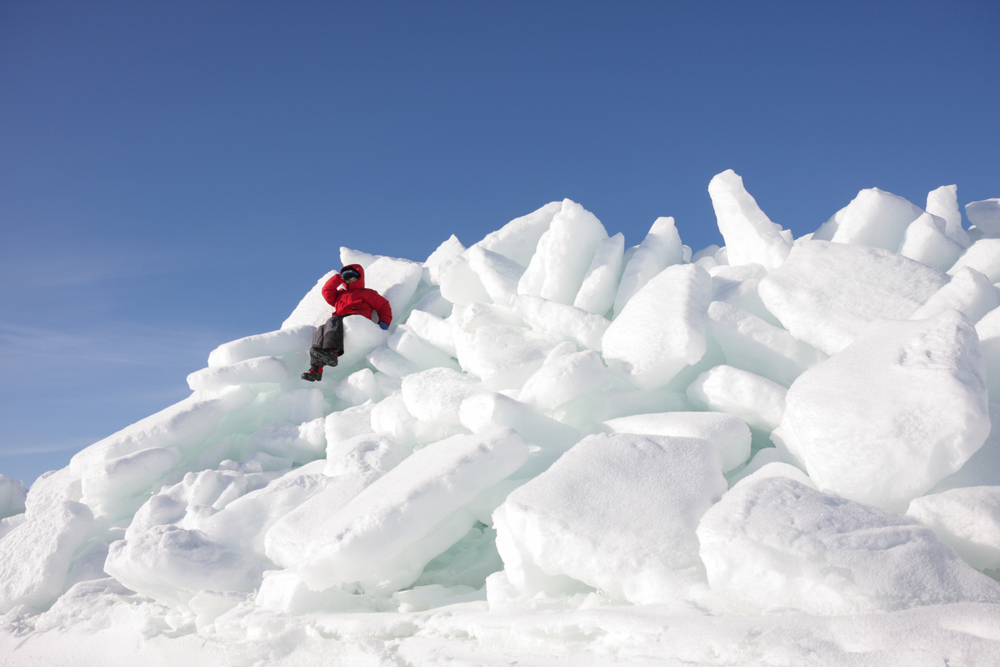 Pileup of ice shove on a shoreline with a kid in a red coat sitting on it.