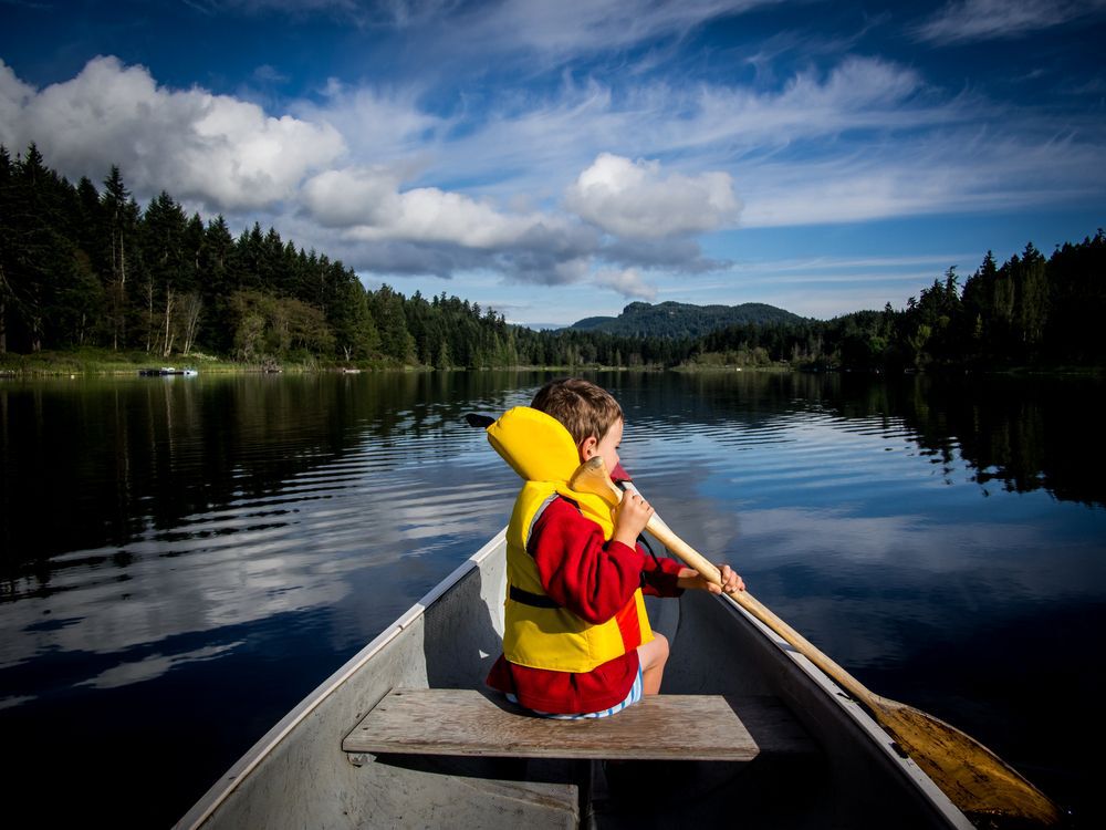 Little kid sitting in a canoe, paddling.