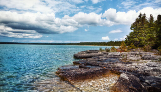 Clear waters of Lake Huron and the rocky shoreline lined with trees.