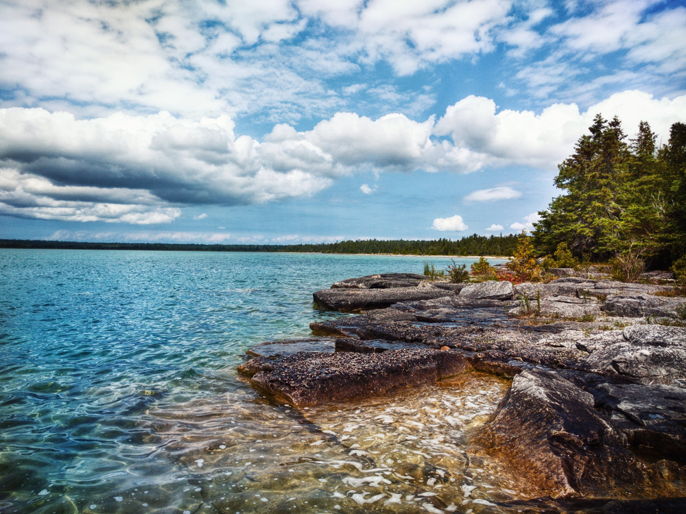 Clear waters of Lake Huron and the rocky shoreline lined with trees.