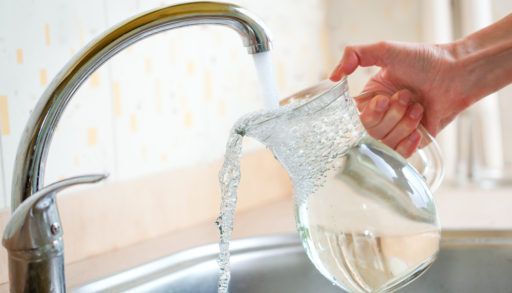 Close-up of a person filling a glass pitcher with tap water.