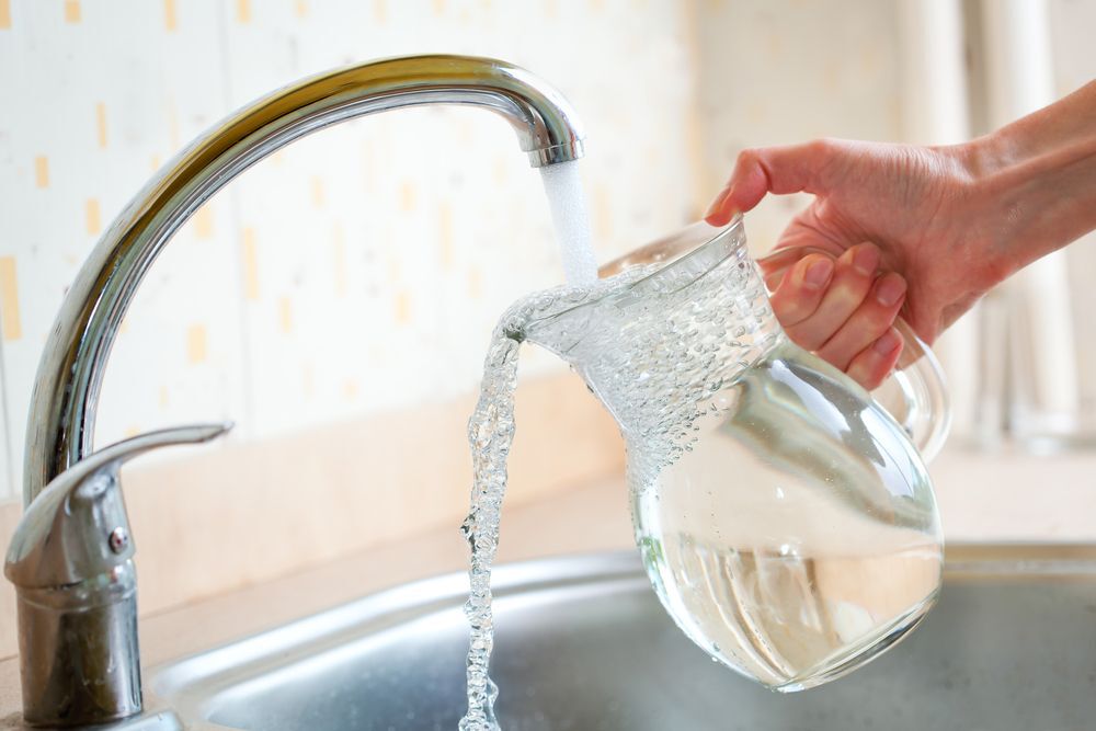 Close-up of a person filling a glass pitcher with tap water.