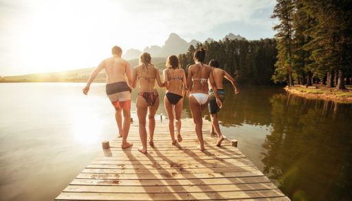 A group of friends jumping off a dock at the lake.