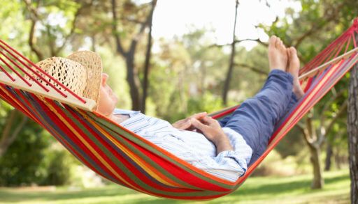 Person wearing a straw hat laying in a red, green, and yellow striped hammock.
