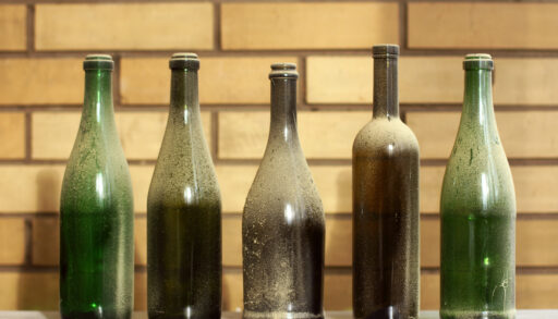 Five old and dusty wine bottles in front of a brick wall.