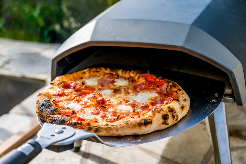 Pizza being taken out of an outdoor pizza oven.