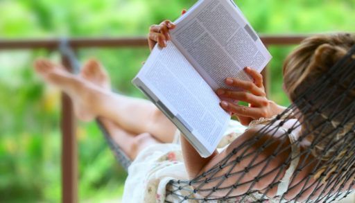 Woman laying on a hammock reading a book.
